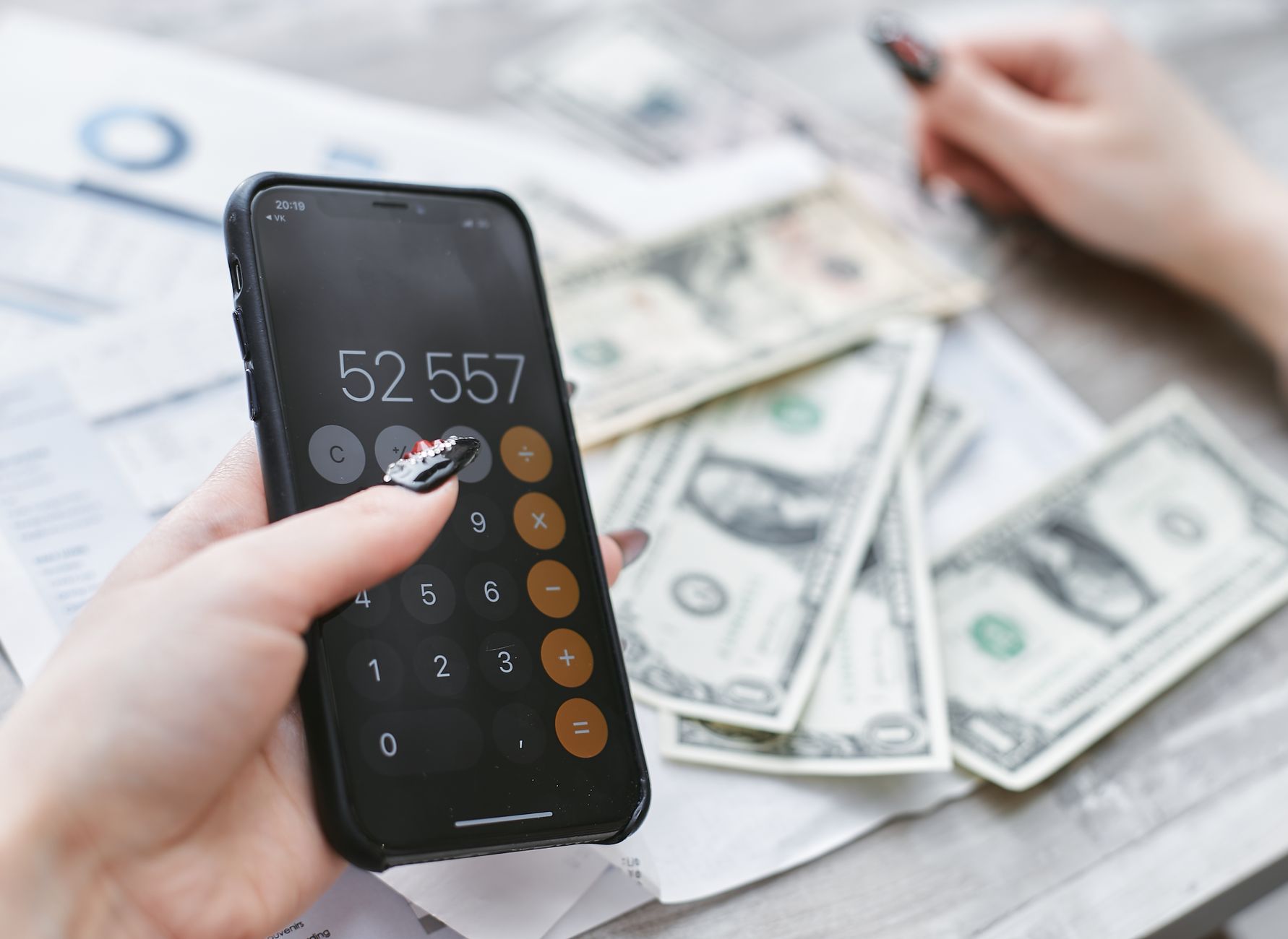 Dłonie liczące na telefonie koszty obok rozłożonych banknotów dolarowych