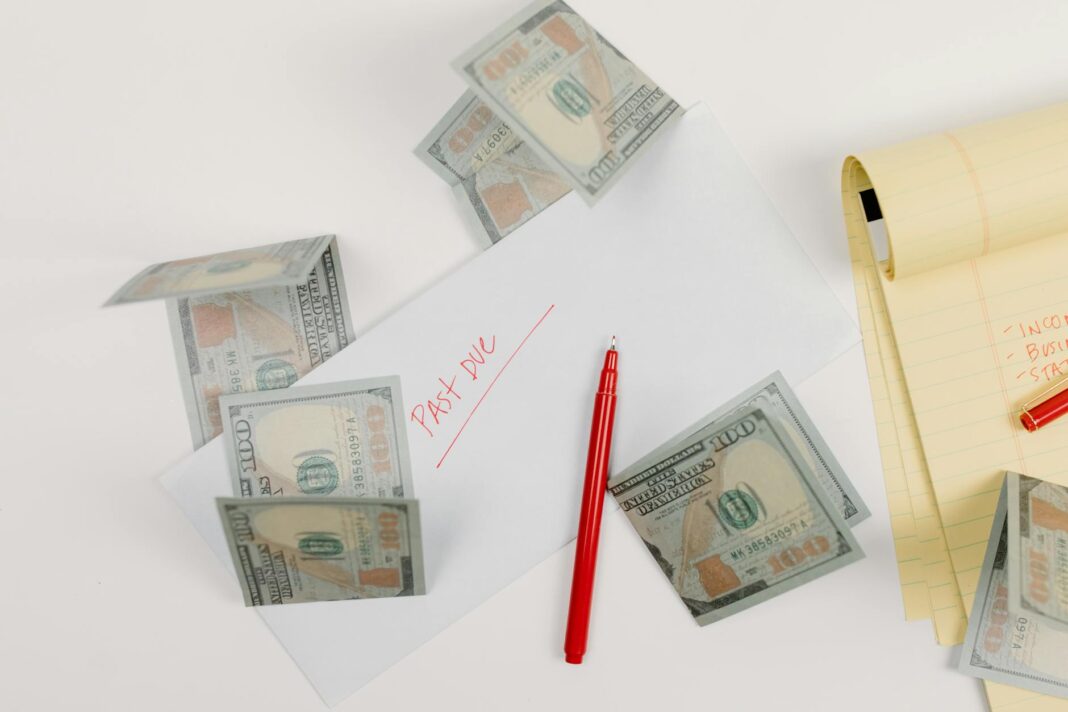 Rozrzucone banknoty dolarów, koperta z napisem past due, notatnik i czerwony dłu