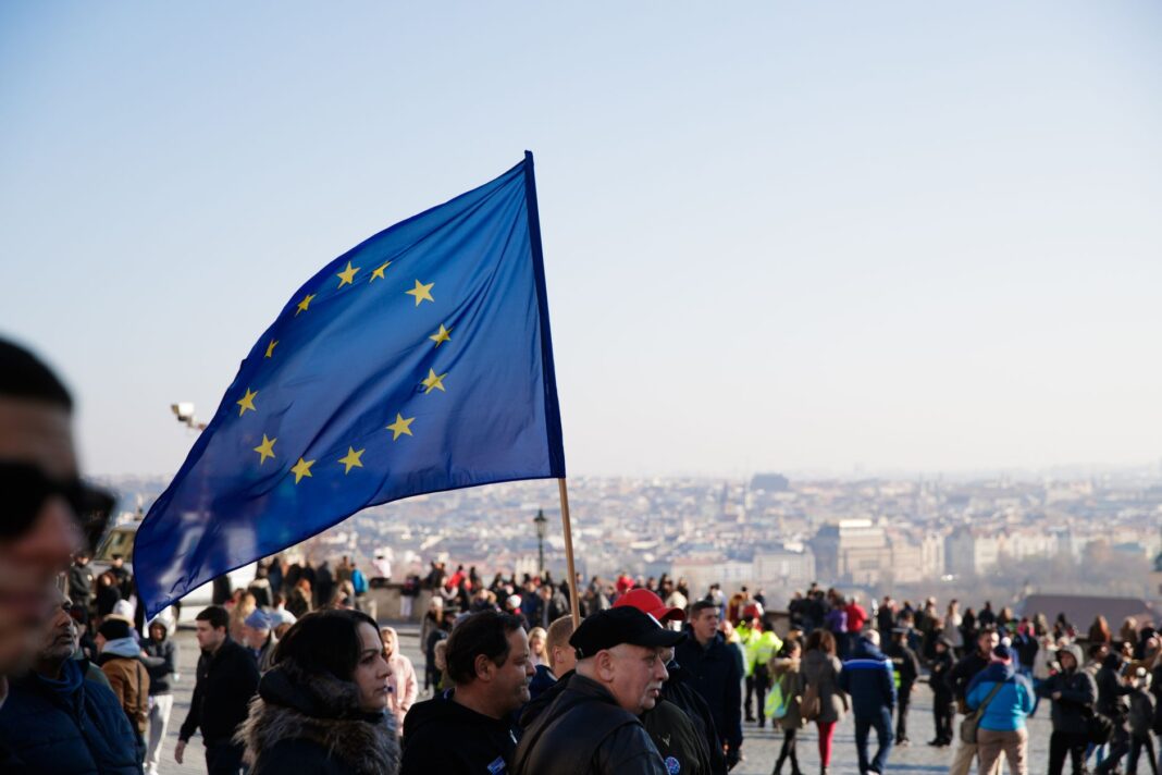 Tłum ludzi idących ulicą z powiewającą flagą Unii Europejskiej
