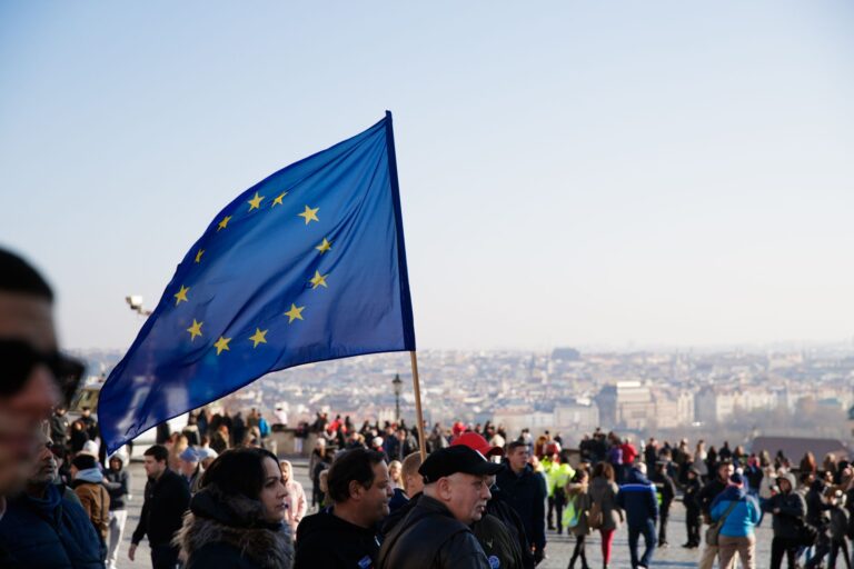 Tłum ludzi idących ulicą z powiewającą flagą Unii Europejskiej