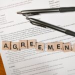 Dokument z napisem AGREEMENT ułożonym z kostek i dwiema długopisami