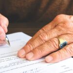 Dłoń seniora z obrączką podpisująca dokument prawny