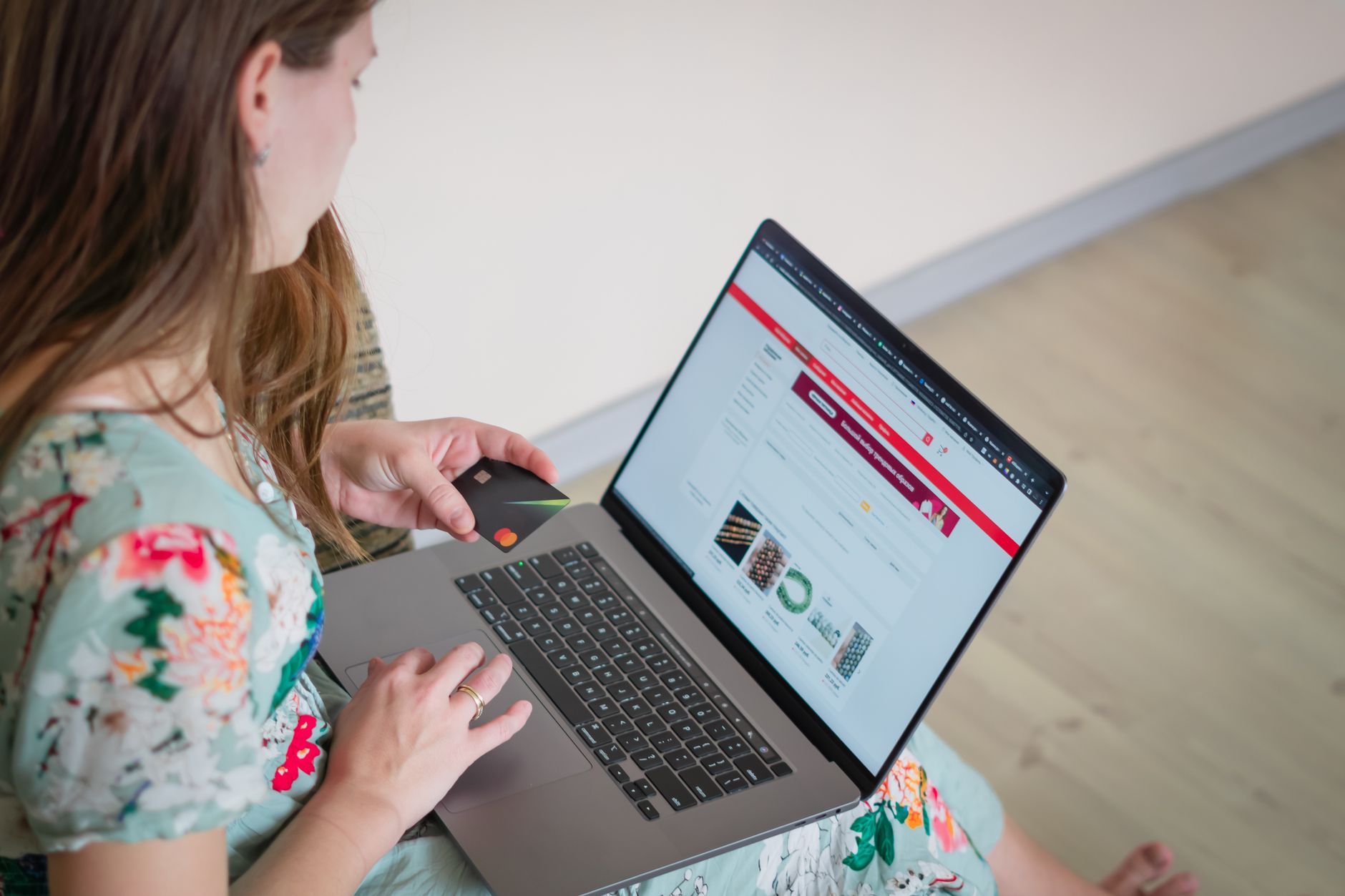 Kobieta w kwiecistej sukience robi zakupy online z kartą przy laptopie