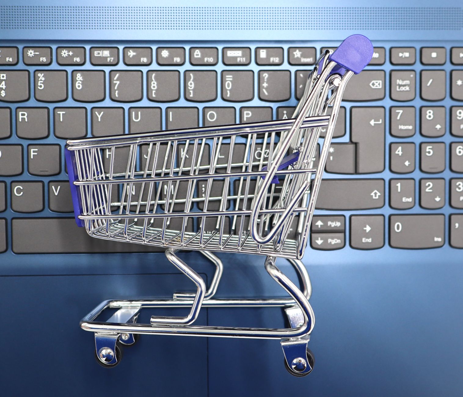 Miniaturowy wózek zakupowy na klawiaturze laptopa symbolizujący e-zakupy
