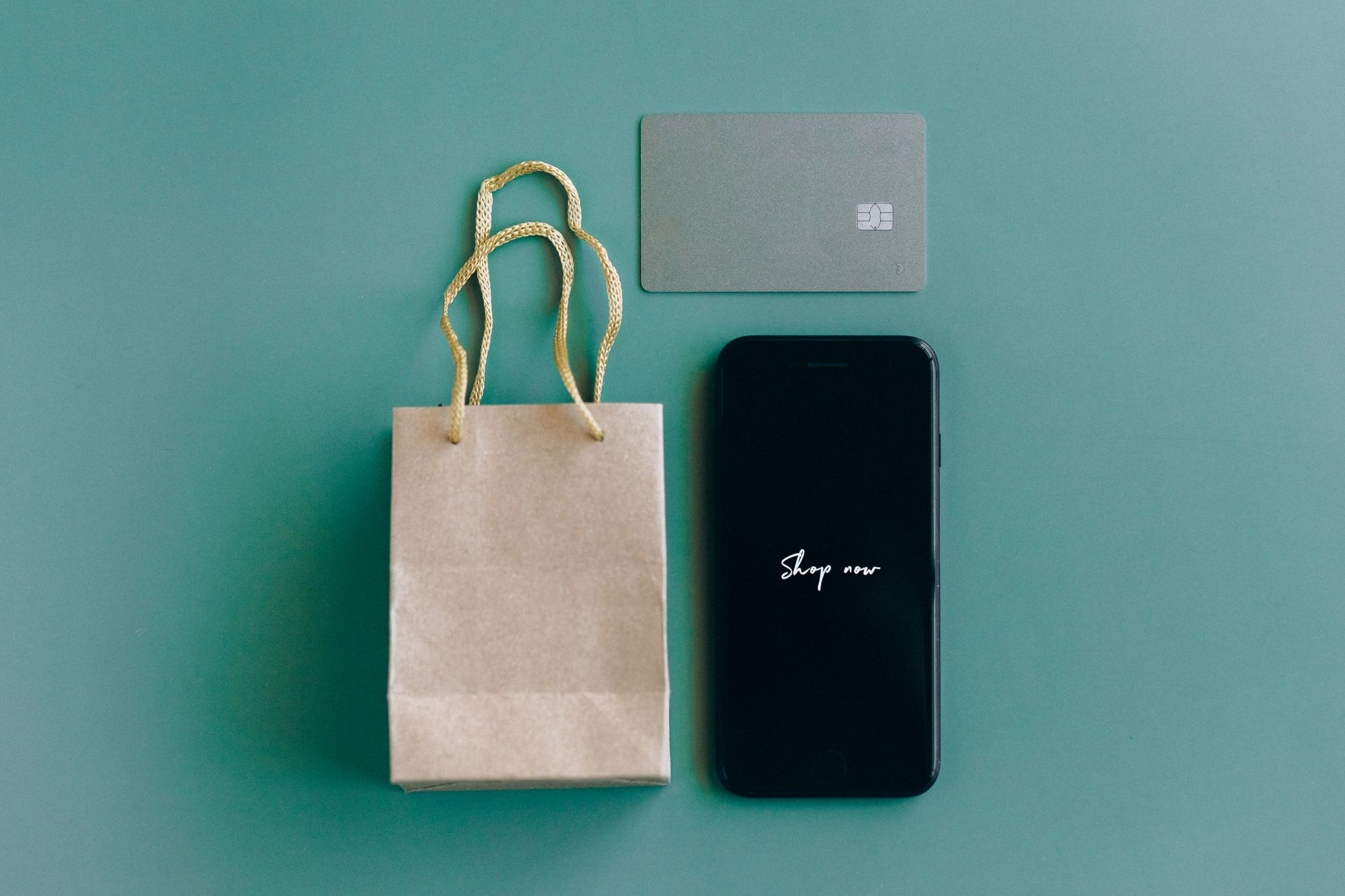 Smartfon z napisem Shop now, karta płatnicza i torba na zielonym tle